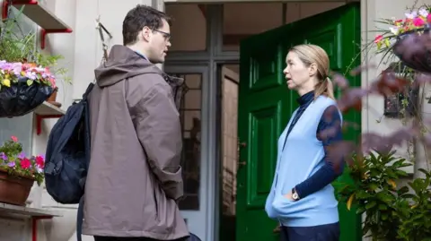 BBC/LA Productions/Kerry Spicer This candid still from the drama shows Bobby Schofield as Joe and Anna Maxwell Martin as Katherine standing in front of a green door, which is open. They are both talking and have their hands in their pockets.
