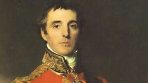 Painting of the Duke of Wellington depicting a head and shoulders in archaic military uniform. Wellington bears a stern face and has black hair 
