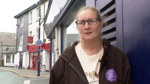 Devon foodbanks say families struggle to feed children in school holidays 1 BBC Chrissie Read has her hair tied back and is standing outside on a pavement leaning against the wall of a shop, wearing glasses, a cream t-shirt and a black hoodie.