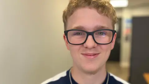 Euan, a boy with short golden hair, wearing a black T-shirt, smiling for the camera. 