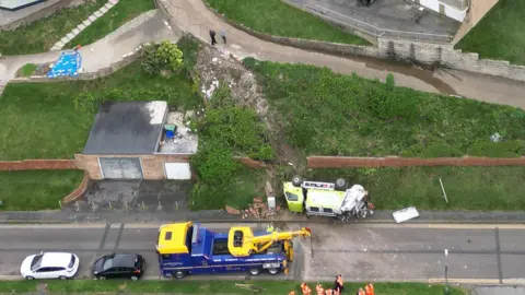 Eddie Mitchell An aerial view of a bin lorry on its side after falling down a grass bank