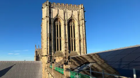 Solar panels on the roof of York Minster, with the sun shining against a blue sky.