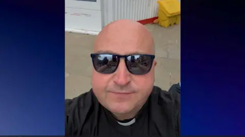 Fr Christopher Woods Father Christopher Woods filming his video near the Botley Road development. He is wearing sunglasses.