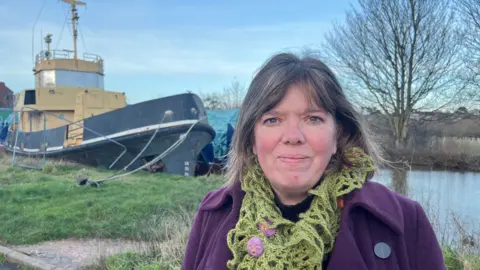 Diana Moore, Green Party leader and ward member, wearing a green scarf and purple coat, standing in front of Exeter canal