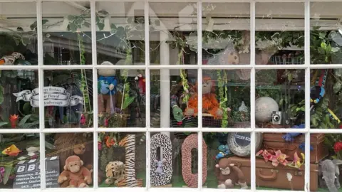 The Yarn Dispensary Sir David Attenborough 100th birthday display in the window of The Yarn Dispensary in Faversham, Kent. A number of animals are in the display, alongside the number '100' created from various type of animal print. 