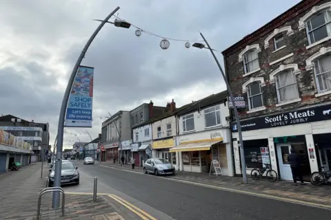 Kevin Shoesmith/BBC News A view of Freeman Street in Grimsby. Shops such as a butcher's and a bakery can be seen beneath a grey sky