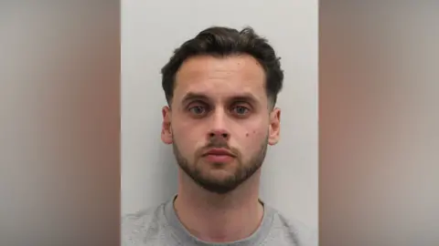 A custody image of a man with dark hair and a close cropped beard looking at the camera. 