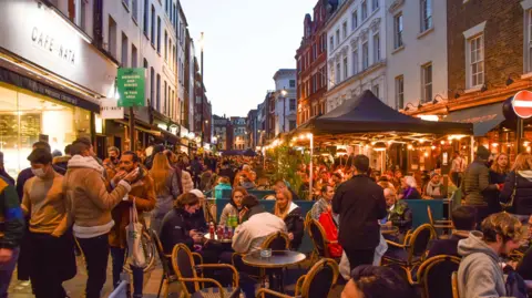 Getty Images People are seated at tables along a street in Soho eating and drinking. 