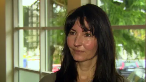 A woman with long brown hair looks off camera