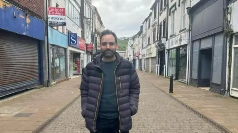 Councillor Joseph Ghayouba standing on King Street with empty shops either side of him. Some of the shutters are rusty and paint is peeling off old signage.