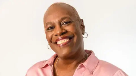 Jennifer Rayner A woman with short hair, hoop earrings and a pink shirt smiling at the camera.