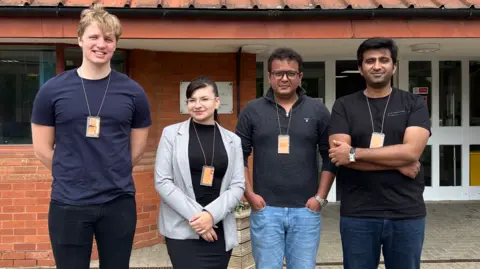 University of Hertfordshire Four students - three men and one woman - are stood together in a line outside a law building wearing lanyards. They are facing the camera.
