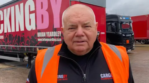 Kevin Hopper, Managing Director of Trucking BY stands in front of one of the company's heavy goods vehicles at the haulage yard in Featherstone 