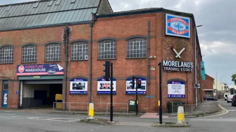 A photo of a red bricked factory with a number of windows and various signs on the wall