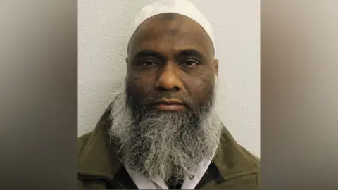 A man with a long grey beard looks at the camera