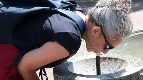 Getty Images Woman sips from a water fountain