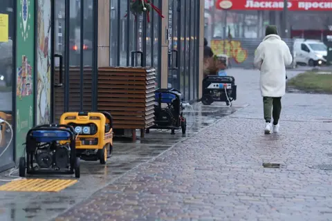 Global Images Ukraine via Getty Images Generators run outside stores during power outages in Dnipro, Ukraine, whilst a person walks past on the pavement 