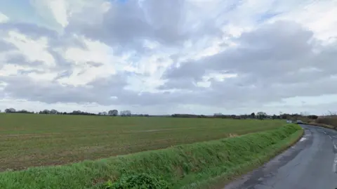 Fields, with a road to the side and grey skies above. 
