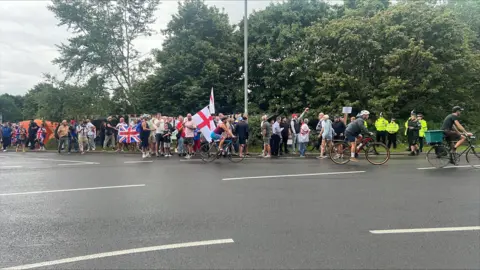 Richard Knights/BBC A large procession of people holding the British flag and the St George flag. There are police officers at the scene