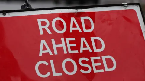 EPA-EFE/REX/Shutterstock Close up of a 'road ahead closed' sign, with white writing on a red background. The sign is slightly battered.