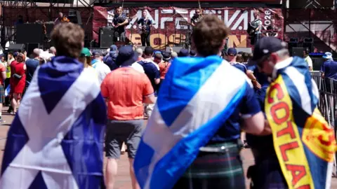 PA Media Fans with Scotland fans watching a concert. There is a band on stage