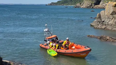 An RNLI lifeboat coming back into shore with a bright yellow kayak attached
