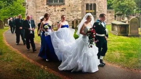Sarah Beavis Sarah Beavis and her husband Michael on their wedding day. Sarah is wearing a white wedding dress and a large veil, while Michael is in military uniform. Her bridesmaids are dressed in blue and they are holding her trail of the dress.