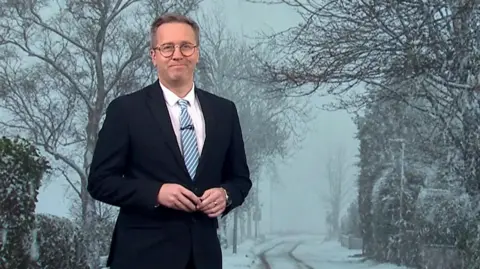 Weather presenter Christopher Blanchett standing in front of a large-scale photograph of wintry conditions