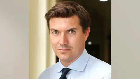 Headshot of James Roscoe wearing a lapis collared shirt. His brown hair slicked to one side.