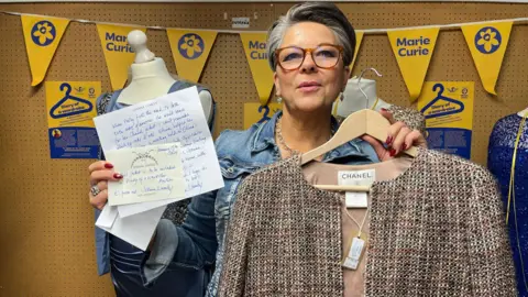 Julia Gregory/BBC The auctioneer holds a Chanel jacket and a letter describing it from Joanna Lumley