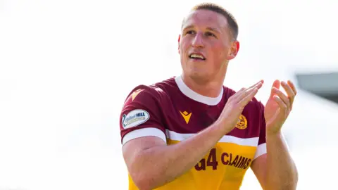 Dan Casey wearing a orange, white and maroon Motherwell shirt while applauding