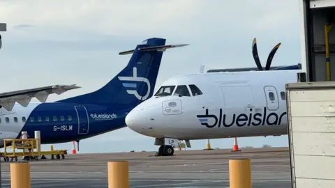 Two Blue Islands aircrafts on the tarmac at Guernsey Airport. Clouded blue skies can be seen behind.