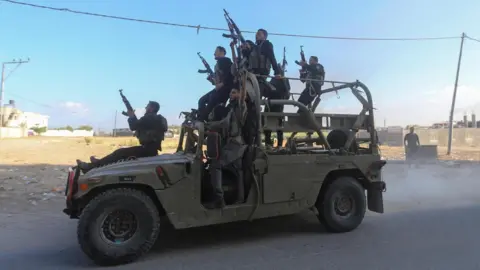 Palestinian gunmen ride an Israeli military vehicle in northern Gaza that was seized during an attack on southern Israel on 7 October 2023