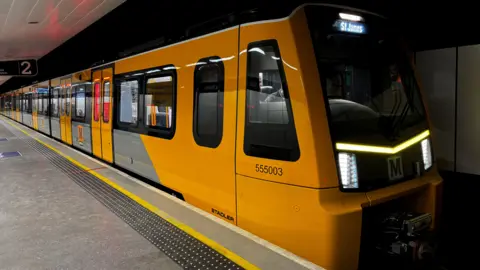 A new Tyne and Wear Metro train has stopped at Platform Two in Central Station, Newcastle, while being tested. It is yellow, black and grey, and is heading towards St James via the coast.