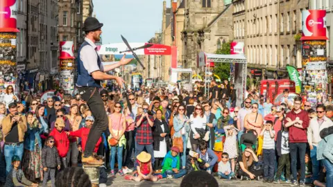 Getty Images A man juggles knives on Edinburgh's Royal Mile, he is surrounded by hundreds of tourists and visitors 