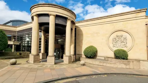 Getty Images Exterior of High Court of Glasgow. A brown stone building with a round, pillared entrance and court of arms on the wall.