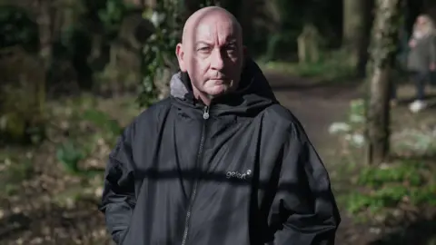 Outreach worker John Heathorn wearing a black coat standing with trees behind him