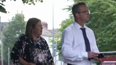 Rebekah Edwards, in a blouse patterned with flowers, and Mark Edwards, in spectacles, white shirt and dark tie, arrive at court