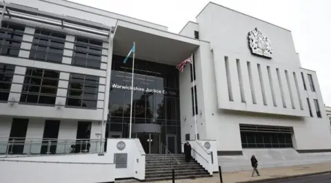 The front of a large white building with black framed windows and doors and steps leading up to a large entrance