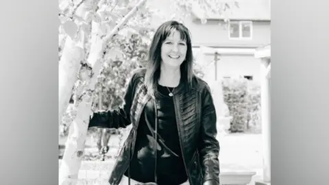 Family A black and white image of a smiling woman with shoulder-length hair wearing a leather jacket and necklace