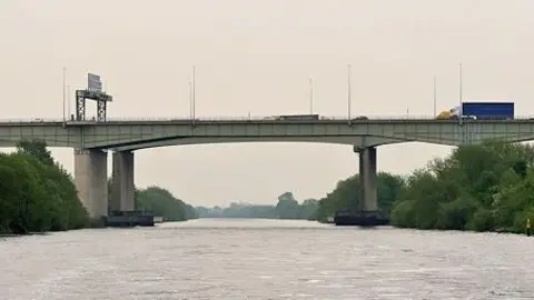 A large grey motorway bridge suspended over a large body of water.