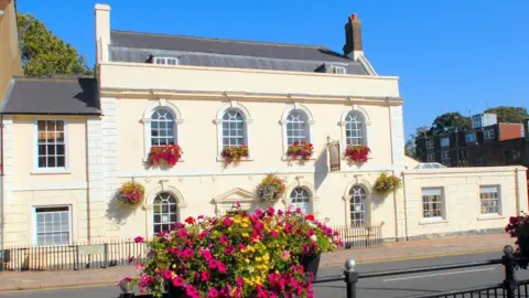 John Chatterley A view of Priory House in Dunstable with a large planter box full of colourful flowers in the foreground