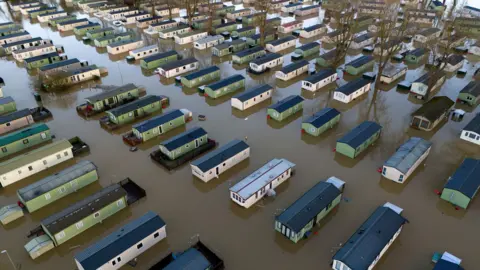 PA Media Flooded caravans at Billing Aquadrome Holiday Park, near Northampton. The homes are surrounded by dark murky water