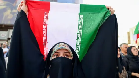 An Iranian woman lifts a national flag during a rally protesting the US attack on Iran in Enghelab Square in Tehran