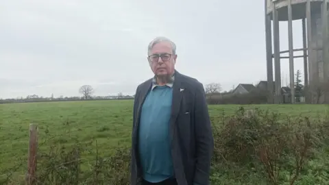 Gavin Grant A man standing in front of field with water tower off to the right