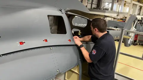 A member of the project team works on the body of the Proteus helicopter inside a hangar.