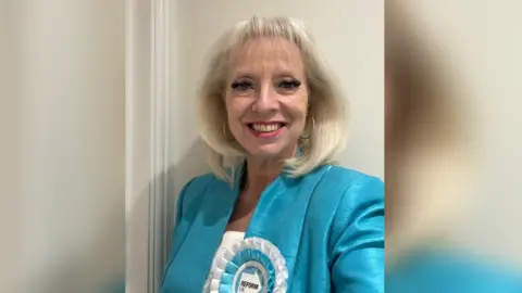 Maxine Fothergill is wearing a turquoise suit with a white and turquoise Reform UK rosette