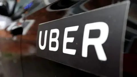 Getty Images A close up of an UBER logo on a sticker on a car door. The lettering is in capitals and in white, and the sticker and car are in black