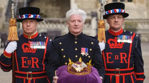 PA Media Former pageant master Bruno Peek standing in the middle of two Beefeaters. On a purple cushion, he is carrying a Diamond Jubilee 'Diamond'. 