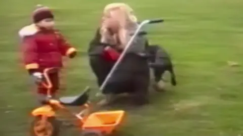 The Murder of Rachel Nickell, Netflix A child stands next to a small tricycle while a blonde woman crouches beside him on the grass.